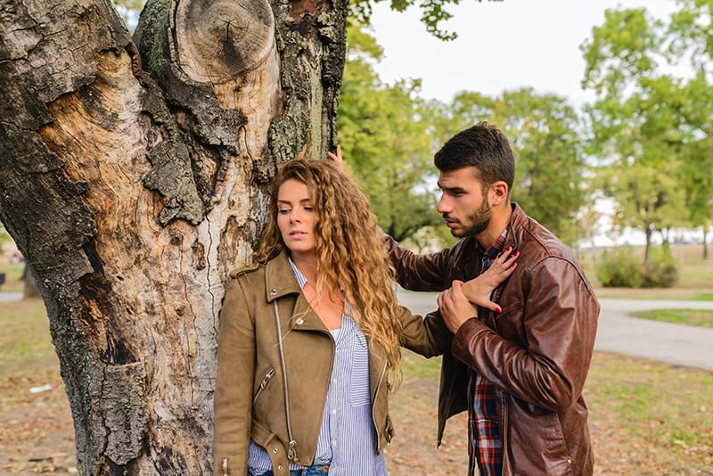 eine Frau, die einen Mann ablehnt, während sie ihn mit einer Hand in den Park drückt