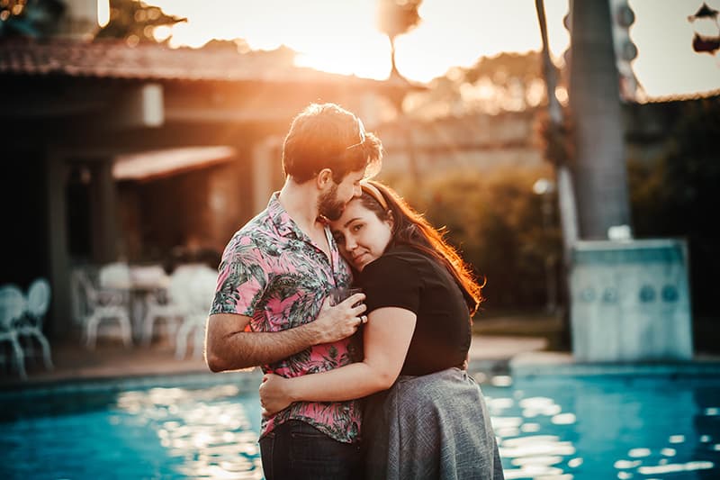 Eine Frau umarmt einen Mann, während ein Mann sie in der Nähe des Schwimmbades auf die Stirn küsst