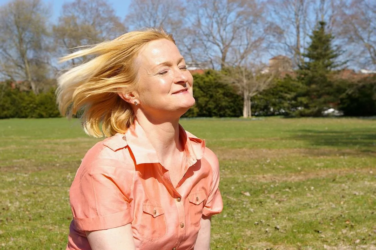 eine Frau mittleren Alters mit geschlossenen Augen, die auf dem Rasen im Park steht