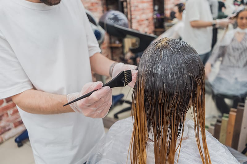 eine Person, die einer Frau in einem Schönheitssalon Haarfärbemittel macht
