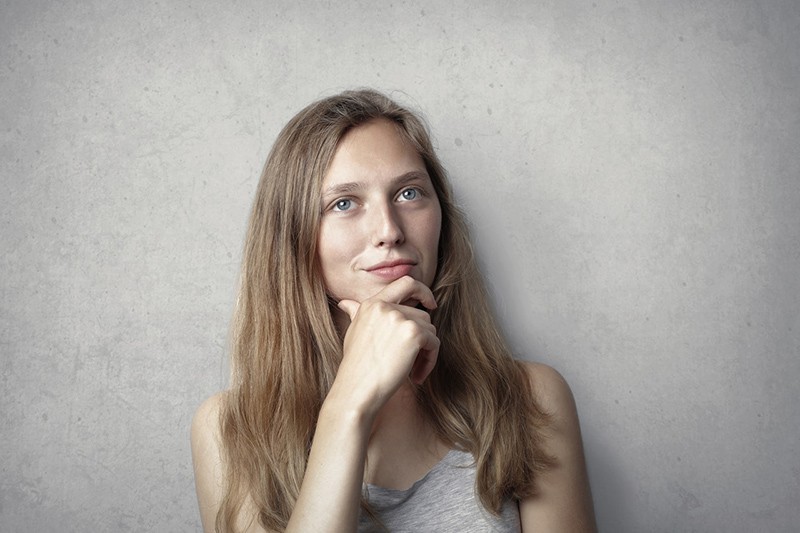 eine entscheidende Frau, die ihr Kinn mit einer Hand berührt, während sie in der Nähe einer grauen Wand steht