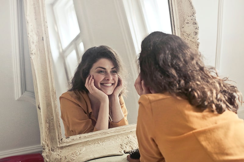 eine glückliche Frau, die sich im Spiegel im Raum ansieht