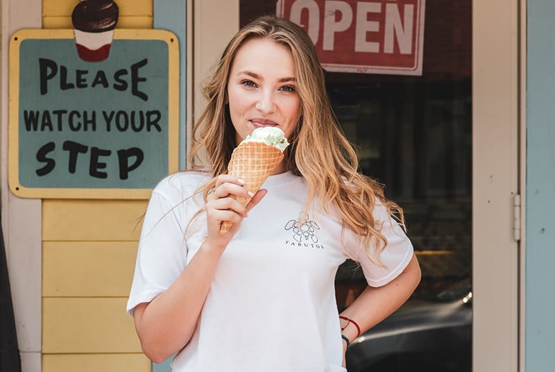 eine lächelnde Frau, die Eis isst, während sie vor dem Laden steht