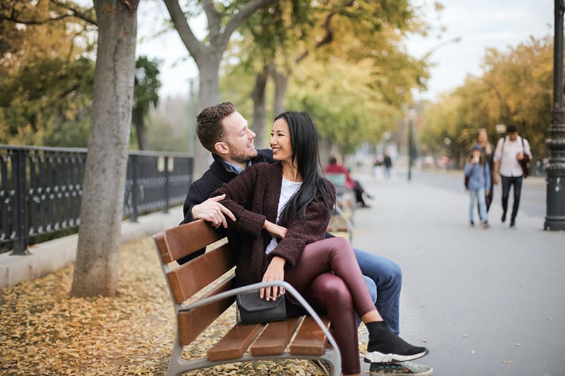 eine lächelnde Frau, die zu einem Mann schaut, während sie zusammen auf der Holzbank sitzt