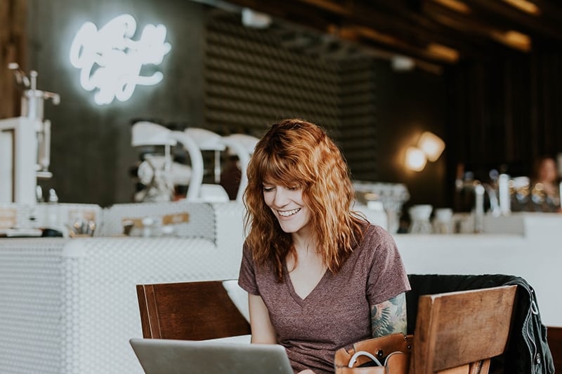 eine lächelnde Frau, die das Internet durchsucht, während sie im Café sitzt