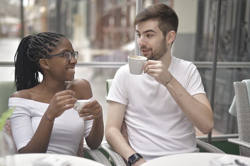 eine lächelnde Frau, die einen Mann beim Kaffeetrinken im Café ansieht