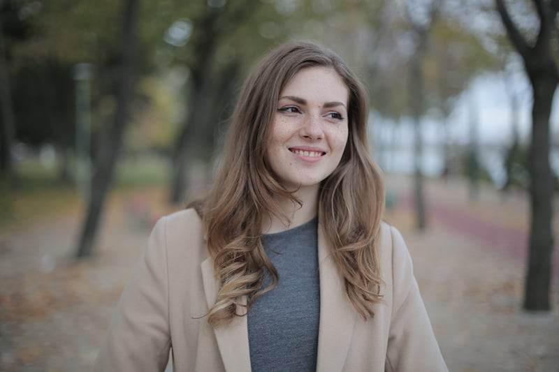 eine lächelnde Frau, die im Park steht, während sie beiseite schaut