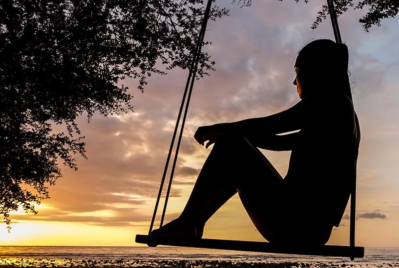 eine nachdenkliche Frau, die auf der Schaukel sitzt und Sonnenuntergang beobachtet