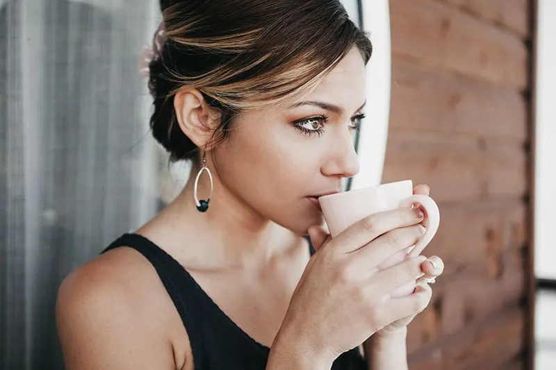 eine nachdenkliche Frau, die einen Kaffee trinkt, während sie draußen steht