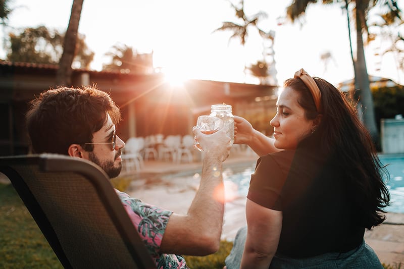eine selbstbewusste Frau, die einen Toast mit einem Mann hat, während sie in der Nähe des Pools sitzt
