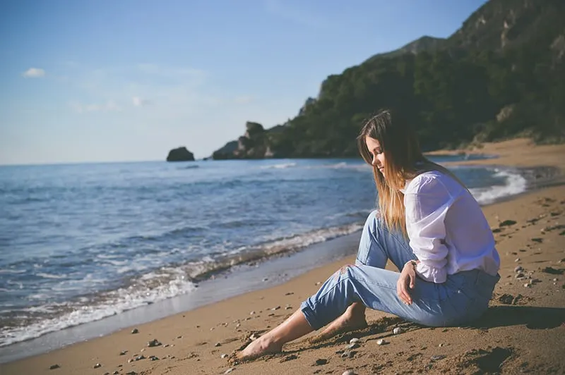 eine traurige Frau, die an der Küste sitzt und in den Sand schaut
