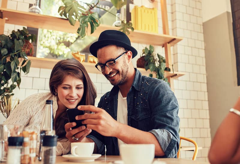 glückliches Paar im Café, das Telefon ansieht
