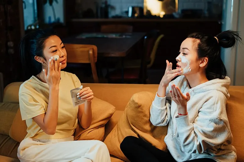 Zwei Frauen tragen eine Gesichtsmaske auf, während sie auf der Couch sitzen