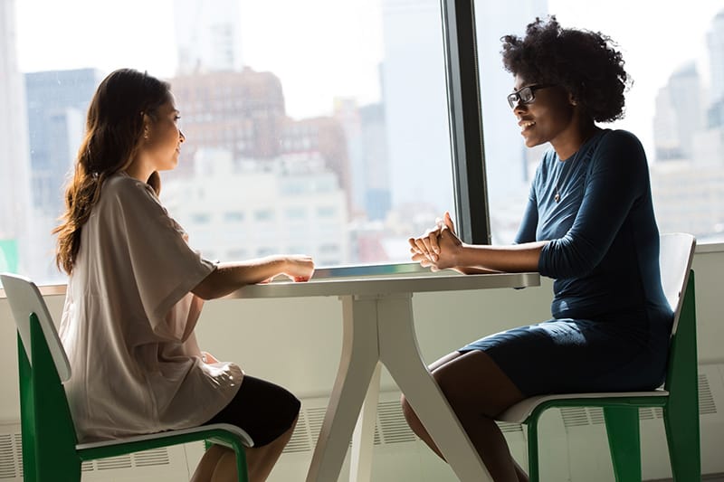 Zwei Frauen unterhalten sich, während sie am Tisch am Fenster sitzen