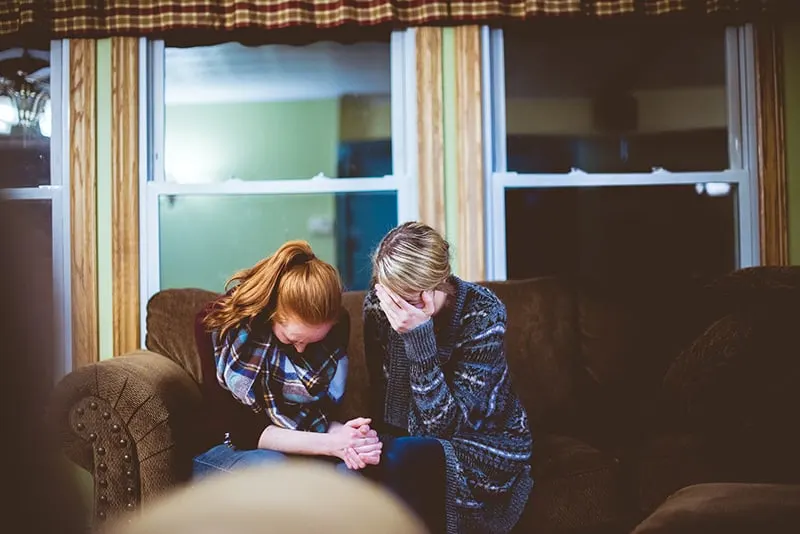 zwei Frauen weinen wegen des Verlustes einer lieben Person, während sie auf dem Sofa sitzen