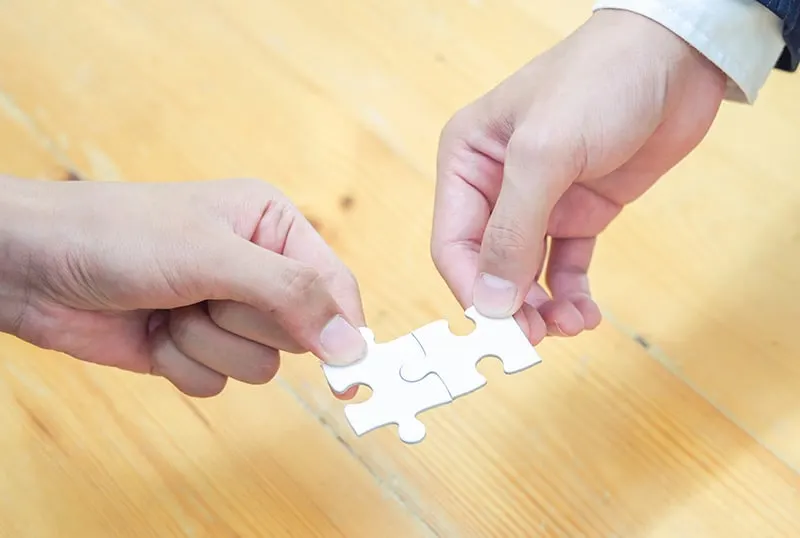 Zwei Personen verbinden zwei Puzzleteile über dem Holztisch