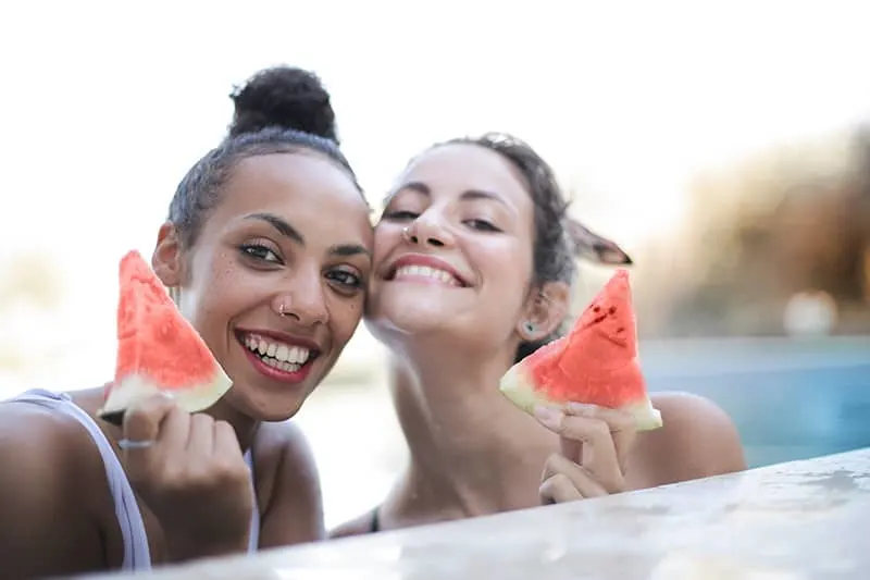 zwei positive Frauen, die eine Wassermelone im Schwimmbad halten