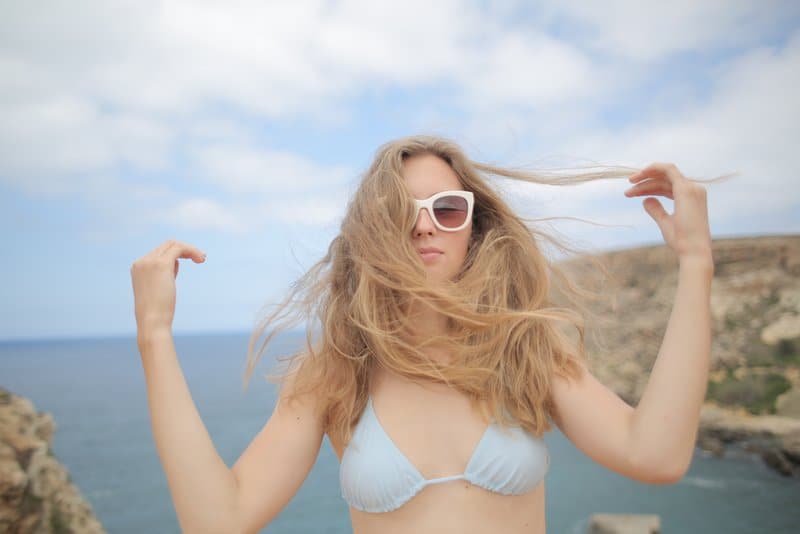 Am Strand steht eine Frau mit Brille und üppigem Haar im Bikini