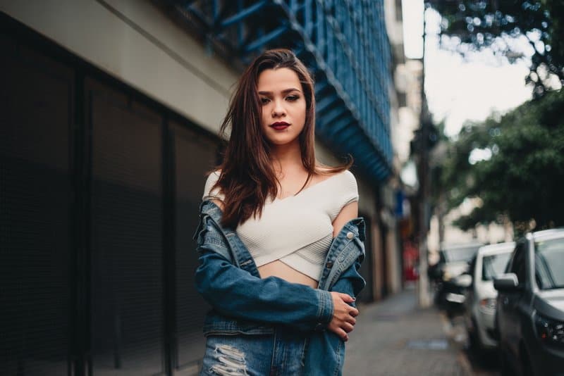 Auf dem Bürgersteig steht ein Mädchen in Jeansjacke und weißem T-Shirt