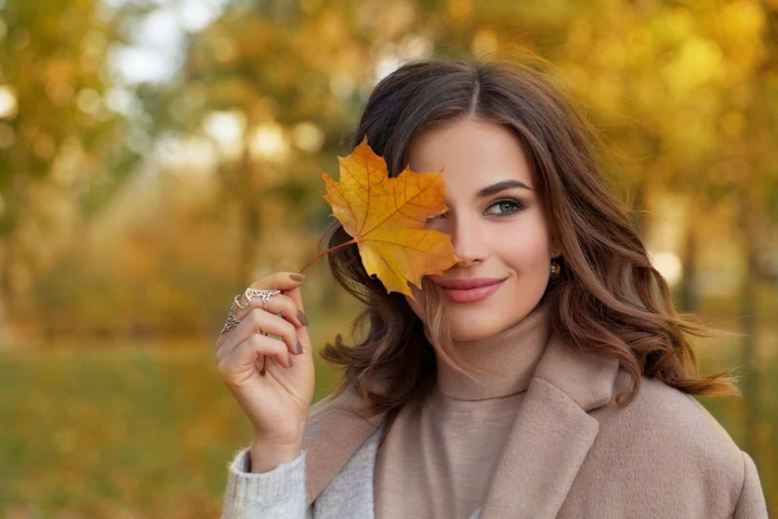 Attraktive Frau hält ein Herbstblatt auf ihrem Auge