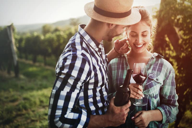Die Frau hält ein Glas in der Hand und lacht, während der Mann eine Flasche hält und die Frau streichelt