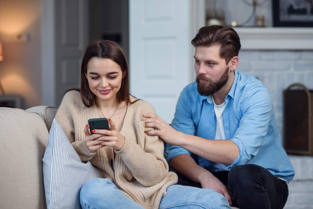 Die Frau sitzt auf der Couch und ignoriert mit einem Lächeln den Mann, der versucht, ihr etwas zu sagen
