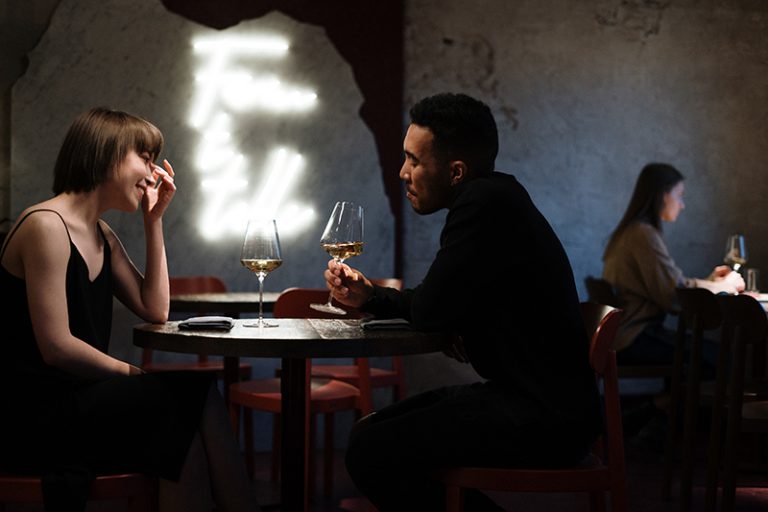 Ein Mann hält ein Glas Wein in der Hand, während er mit einer Frau in einem Restaurant spricht
