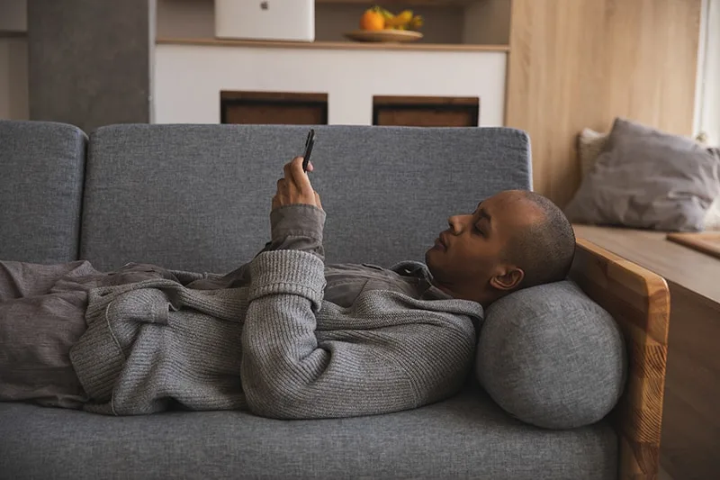 Ein Mann, der sich auf der Couch entspannt und ein Smartphone benutzt