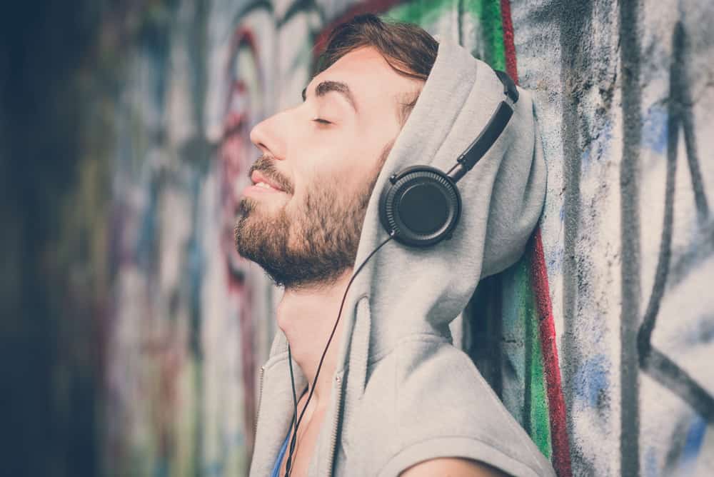 Ein Mann mit Bart, der an eine Wand gelehnt ist, hört Musik über Kopfhörer