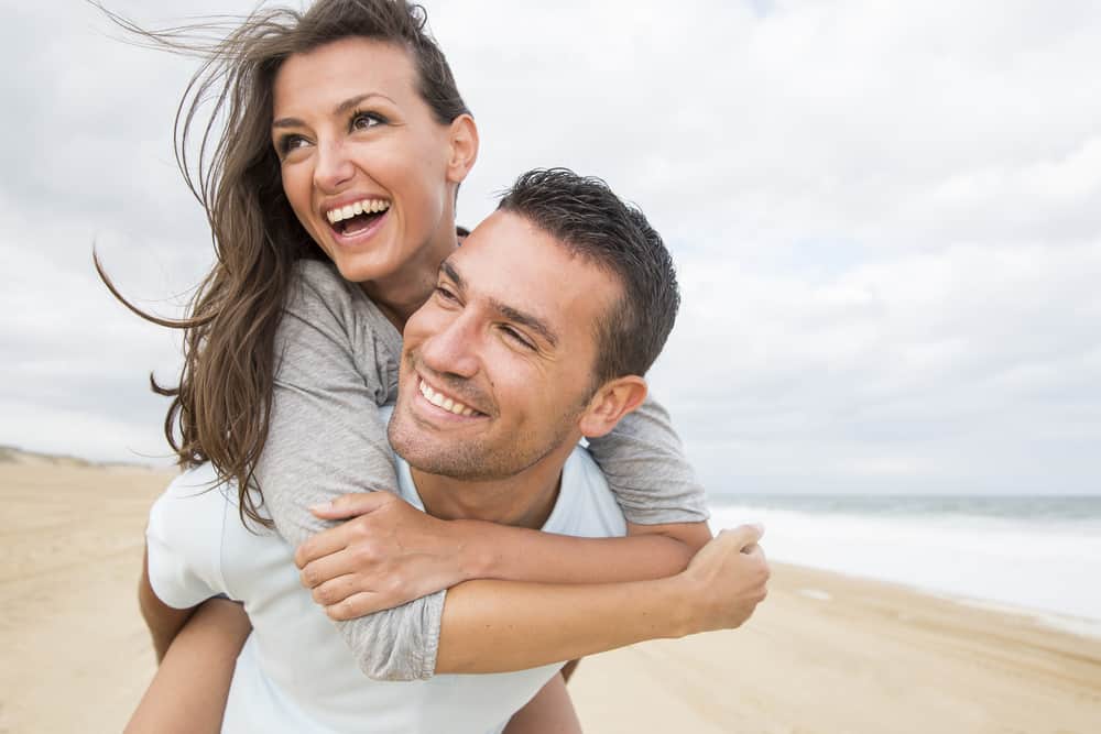 Ein Mann trägt eine Frau zum Strand und sie lachen