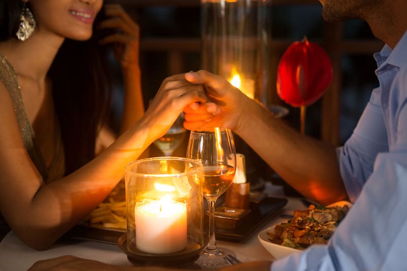 Ein Mann und eine Frau halten sich bei romantischem Abendessen bei Kerzenlicht die Hände zusammen