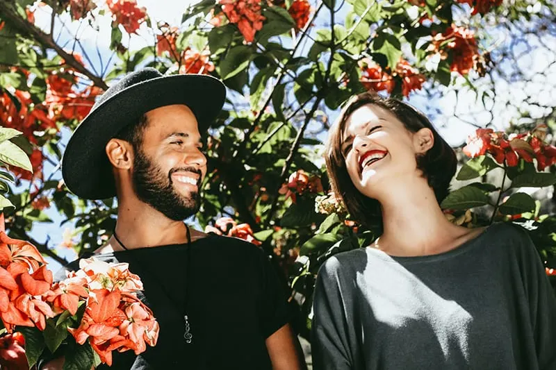 Ein Mann und eine Frau lachen zusammen, während sie in der Nähe der Blumenbäume stehen