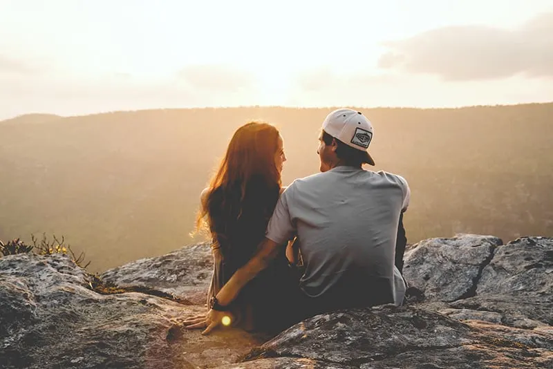 Ein Mann und eine Frau schauen sich an, während sie während des Sonnenuntergangs auf der Klippe sitzen