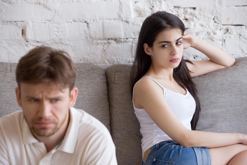 Ein frustriertes Mädchen in kurzen Hosen sitzt auf der Couch und beobachtet ihren wütenden Mann