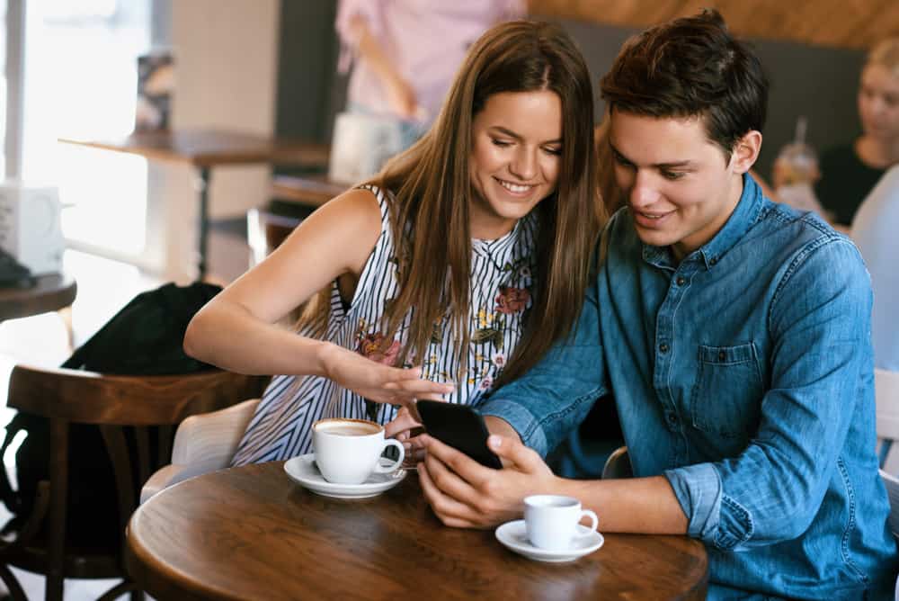 Ein junges Liebespaar sitzt in einem Café und schaut sich etwas auf ihrem Handy an