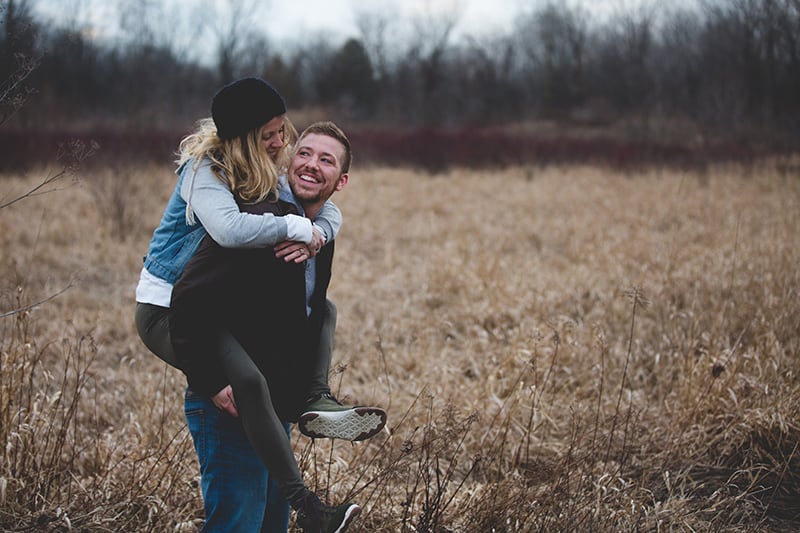 Ein lächelnder Mann trägt eine Frau auf dem Rücken, während er auf dem Feld steht