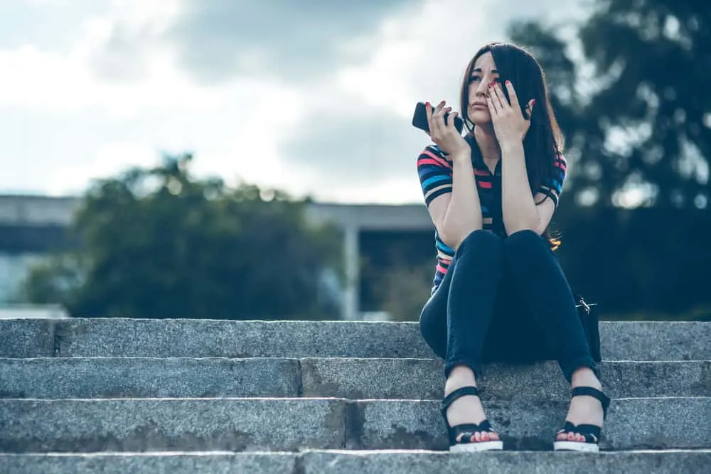 Eine Frau mit einem Handy in der Hand sitzt auf der Treppe und weint