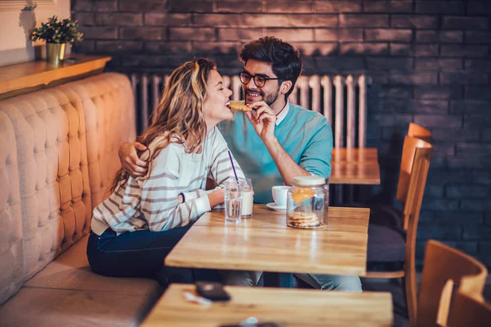 Eine glückliche Frau isst in einem Café einen Keks aus der Hand ihres Mannes