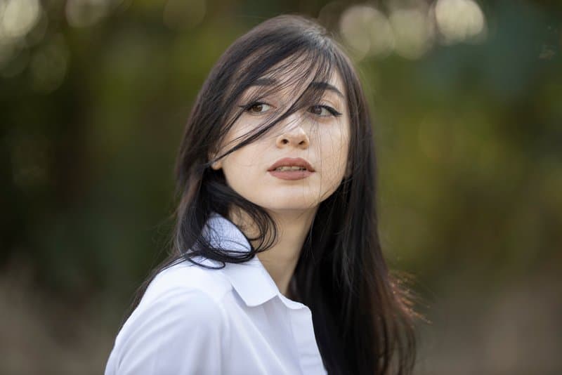 Eine schwarzhaarige Frau in einem weißen Hemd steht draußen und schaut über die Schulter