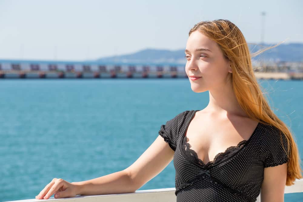 Eine schöne Frau in einem schwarzen Kleid steht an einem Zaun in der Nähe des Meeres