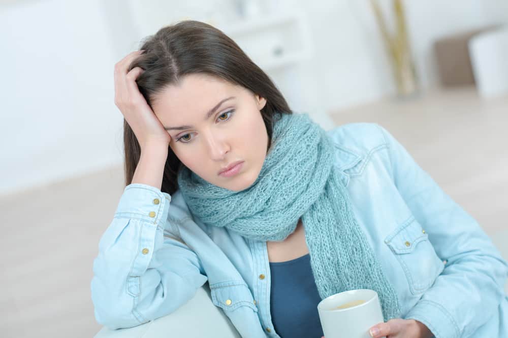 Eine traurige Frau mit einem Schal um den Hals sitzt und denkt über Kaffee nach
