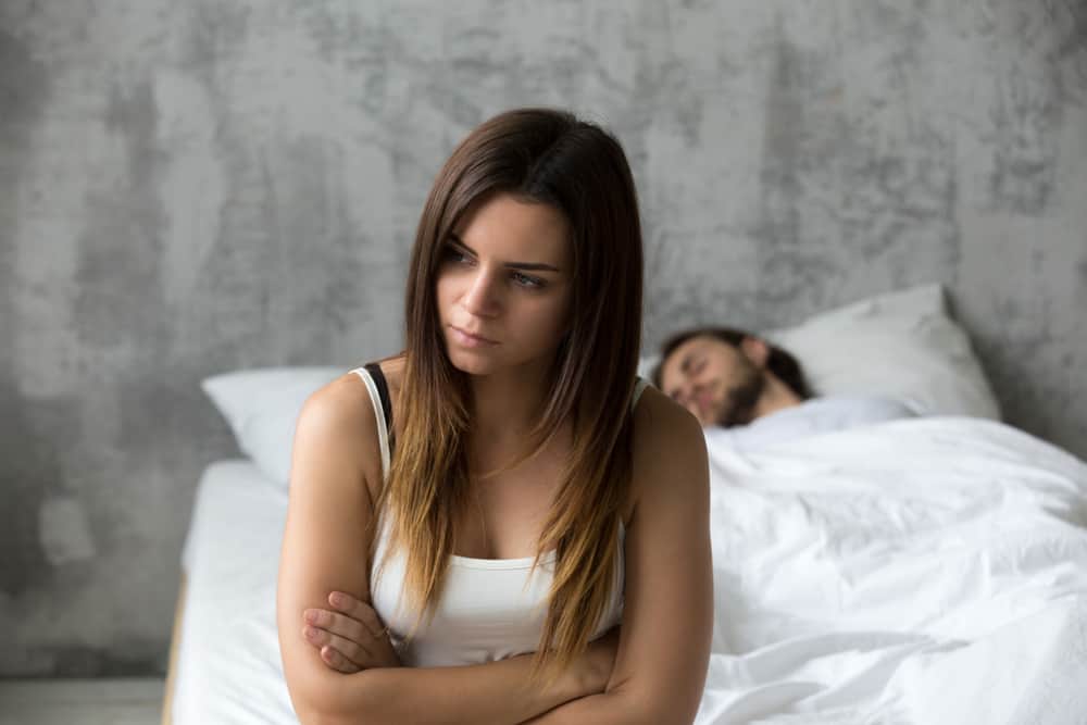 Eine wütende Frau sitzt auf dem Bett, während ihr Mann sorglos schläft
