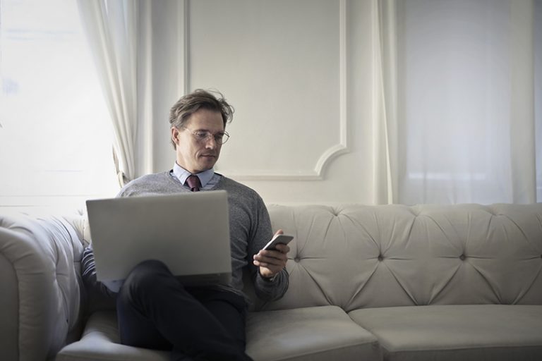 ein Mann, der Telefon während der Arbeit am Laptop betrachtet
