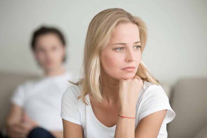 Ernsthafte traurige Frau, die über ein Problem nachdenkt, während ein Mann hinter ihr sitzt