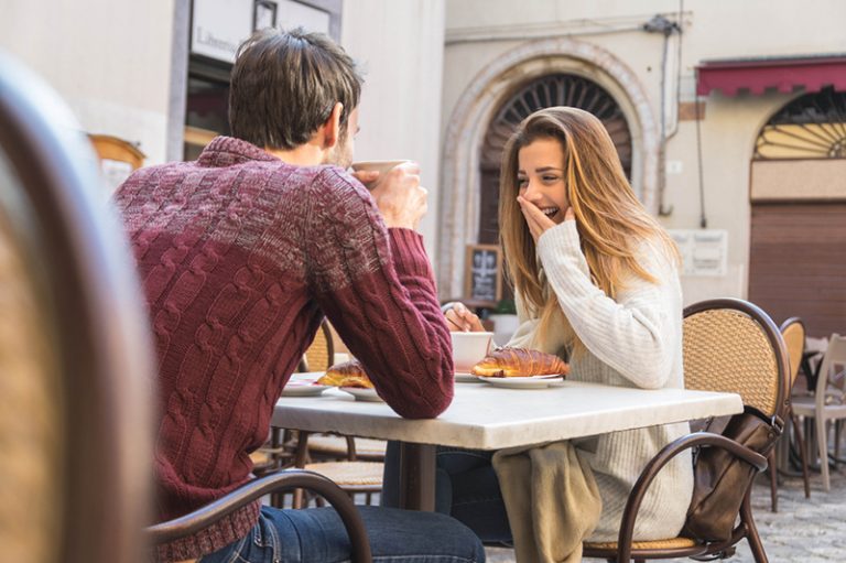 Ein Mann und eine Frau lachen beim gemeinsamen Frühstück im Café