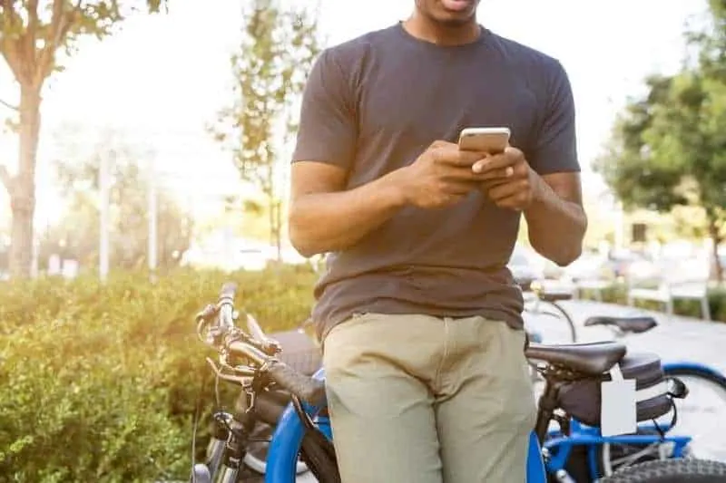 Mann, der auf seinem Telefon tippt, während er sich auf Fahrrad stützt
