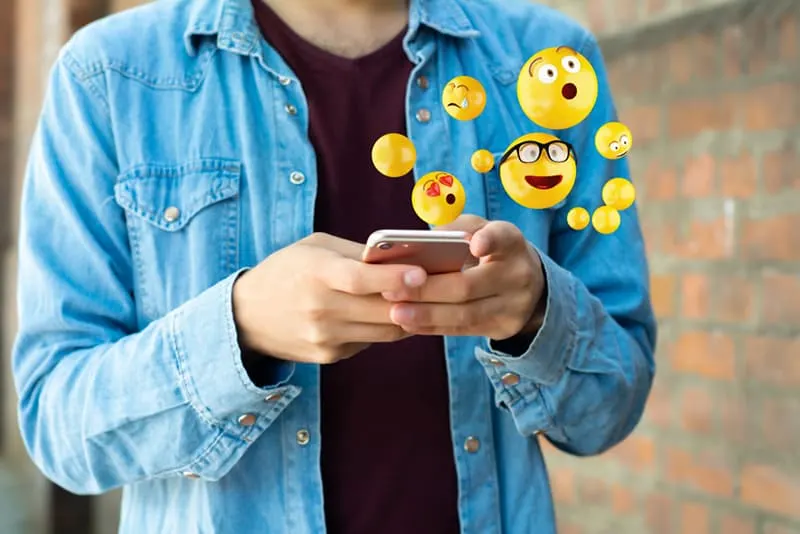 Mann mit Smartphone und Emojis senden, während in der Nähe der Wand stehen