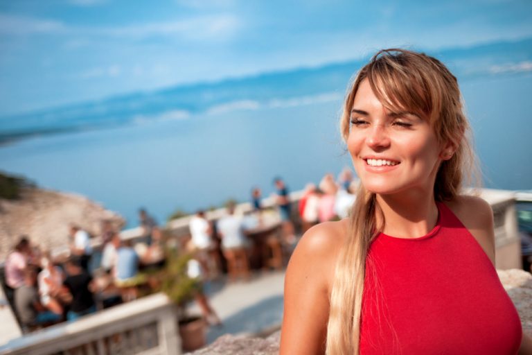 Über dem Strand steht ein lächelndes Mädchen in einem roten T-Shirt