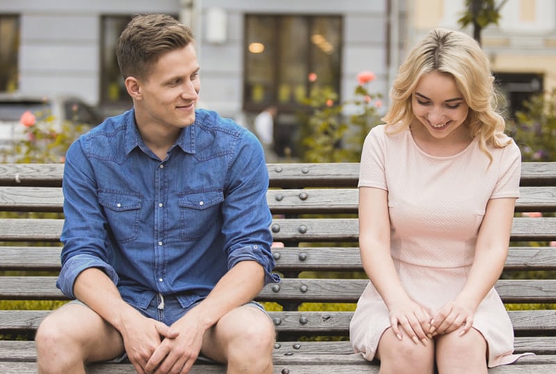 attraktiver Kerl, der mit einer schönen Frau flirtet, während er zusammen auf der Bank sitzt