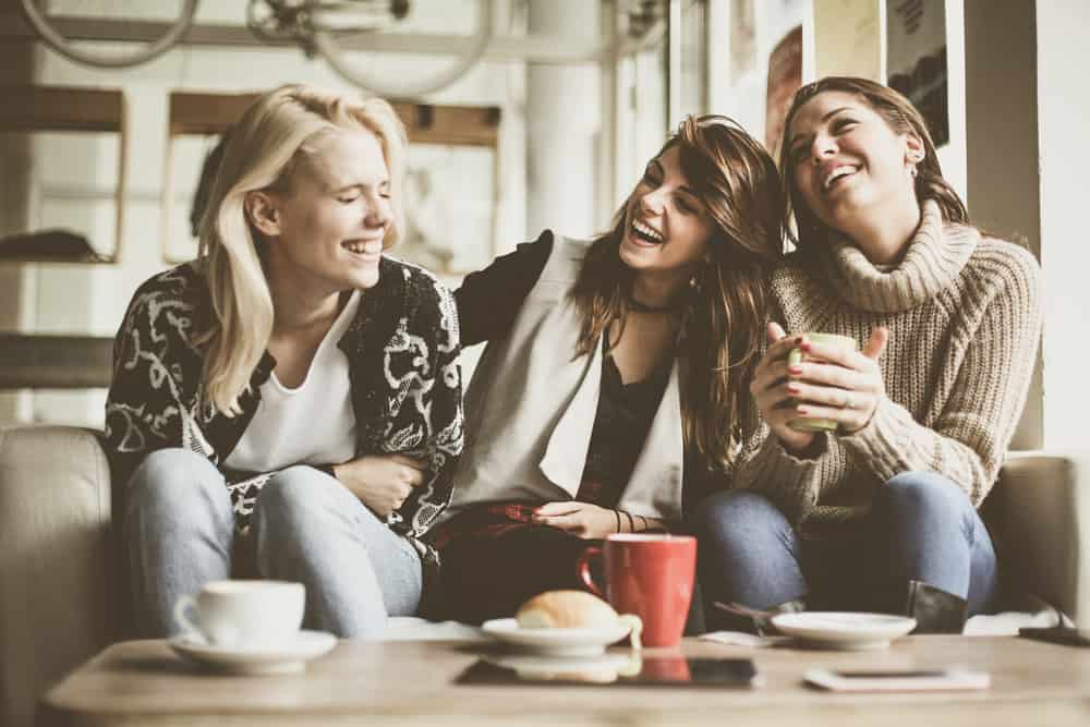 drei lächelnde Freunde, die zu Hause Kaffee trinken